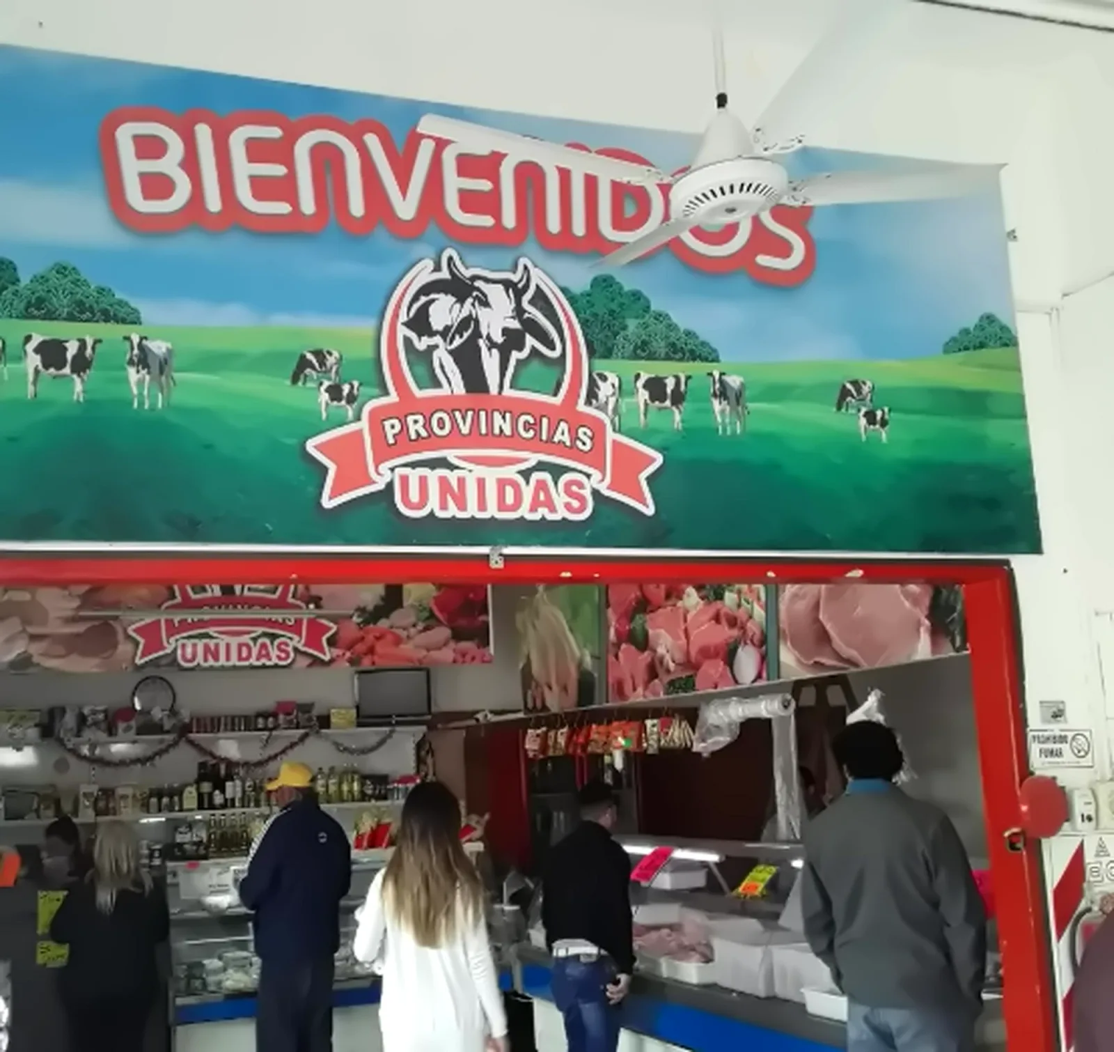 Cartel de bienvenida de la carnicería Provincias Unidas con su logo sobre un paisaje de campo con vacas